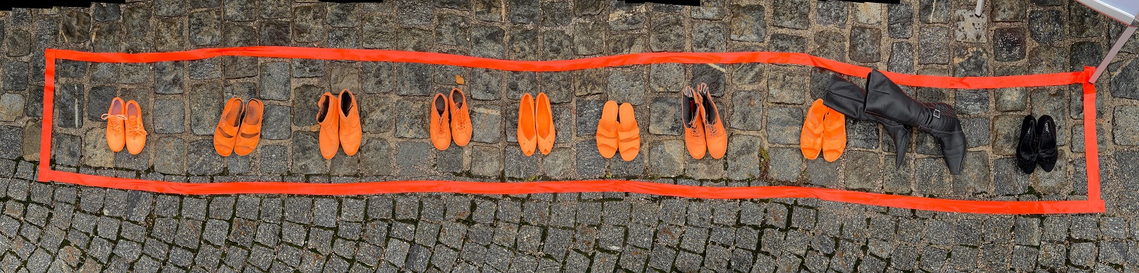 Schuhe in Orange und Schwarz in einer Reihe umgeben von Rand in Orange. Aufgenommen auf Pflastersteinen